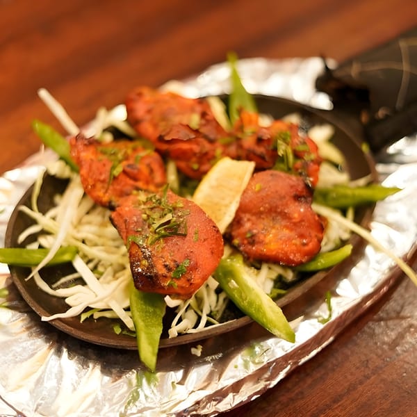 Indian chicken tikka, garnished with cilantro and lemon, served on a sizzling platter with cabbage and peppers.
