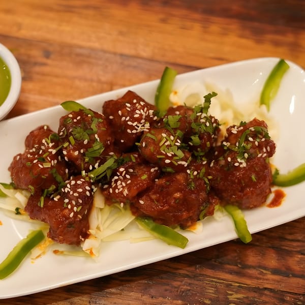 Indian chili chicken with sesame seeds and cilantro on a white plate with green peppers.